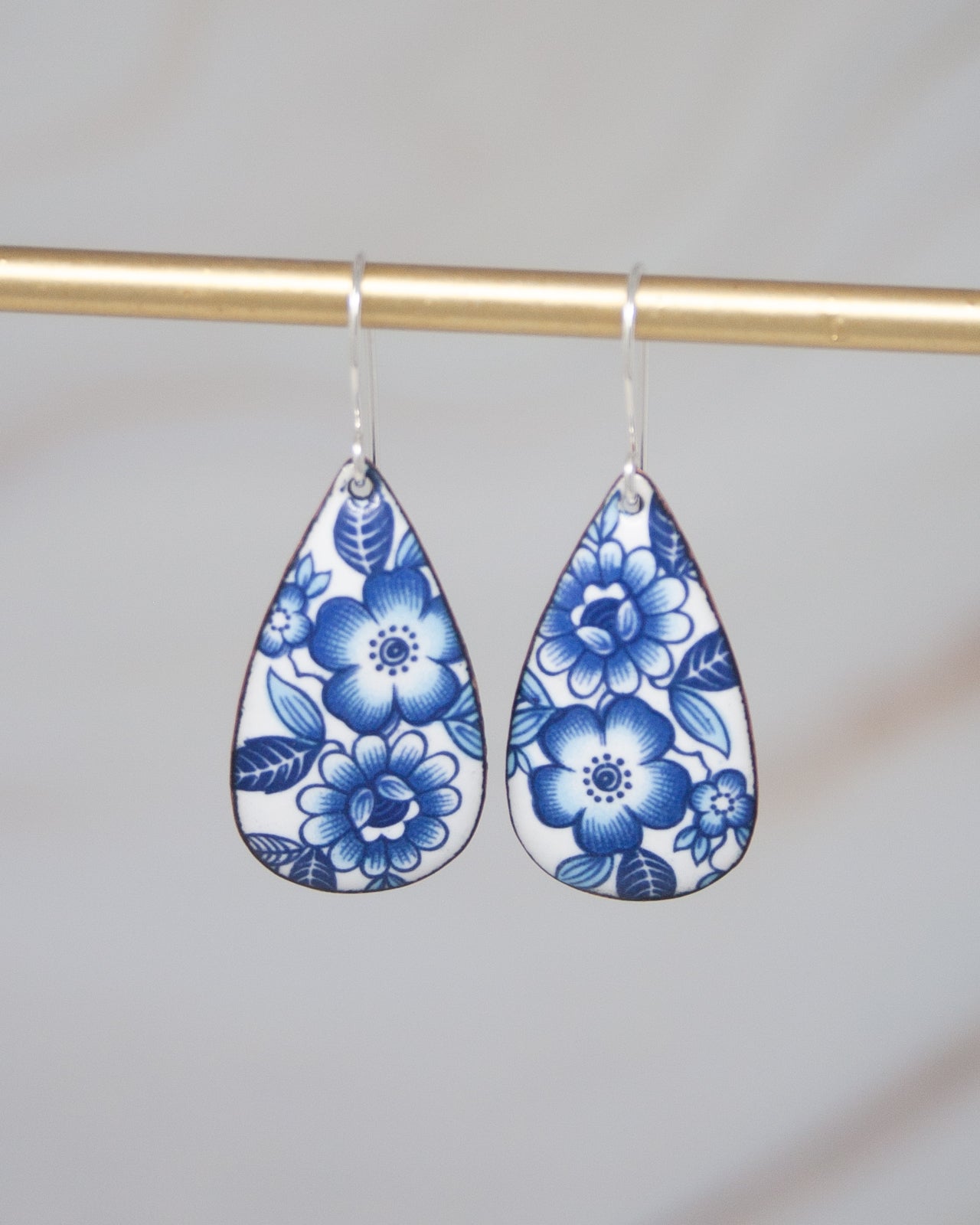A pair of earrings with blue floral designs hanging from a gold bar.