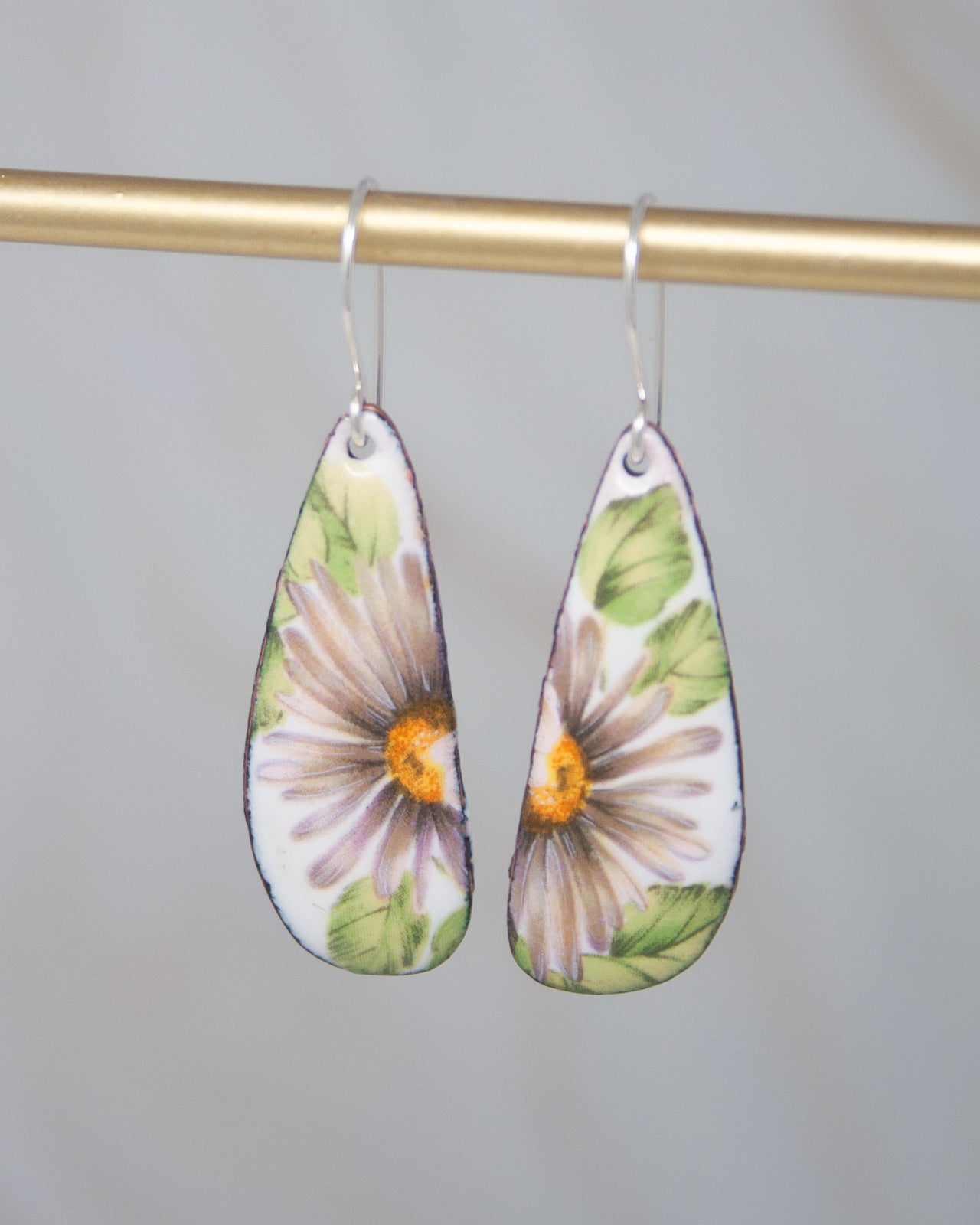 A pair of earrings with a floral design, featuring a white background with green and orange flowers.