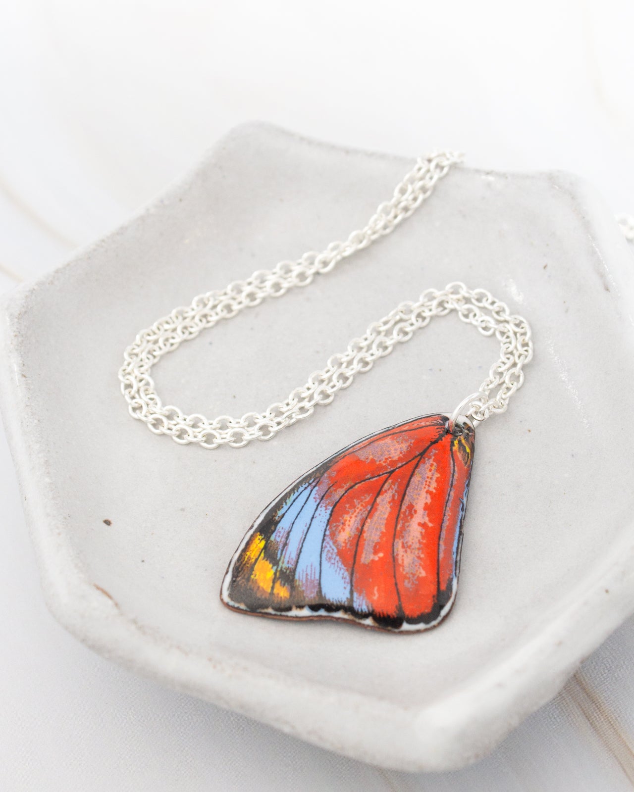 A necklace with a pendant in the shape of a colorful butterfly rests on a white plate.