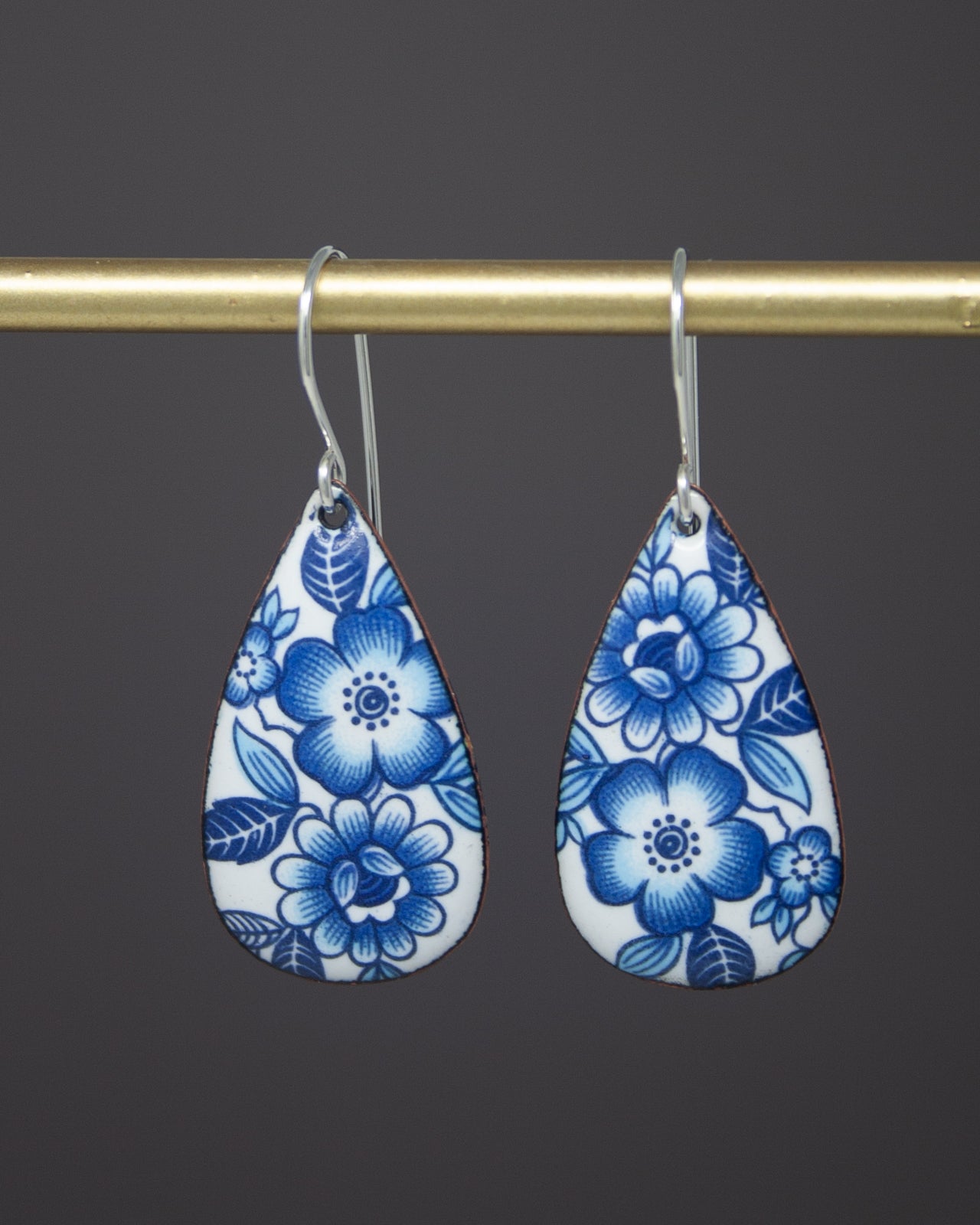 A pair of blue and white floral earrings hanging from a gold bar.