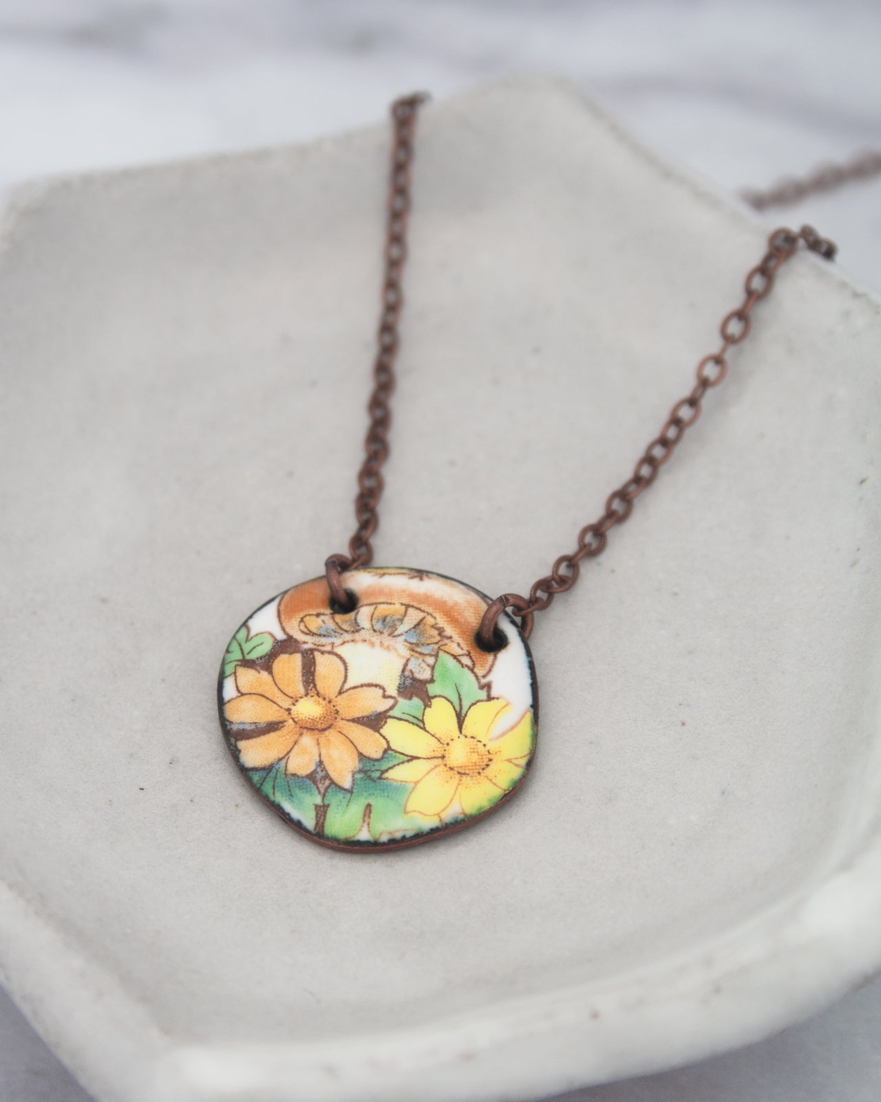 A necklace with a circular pendant featuring a floral design in shades of yellow and orange.