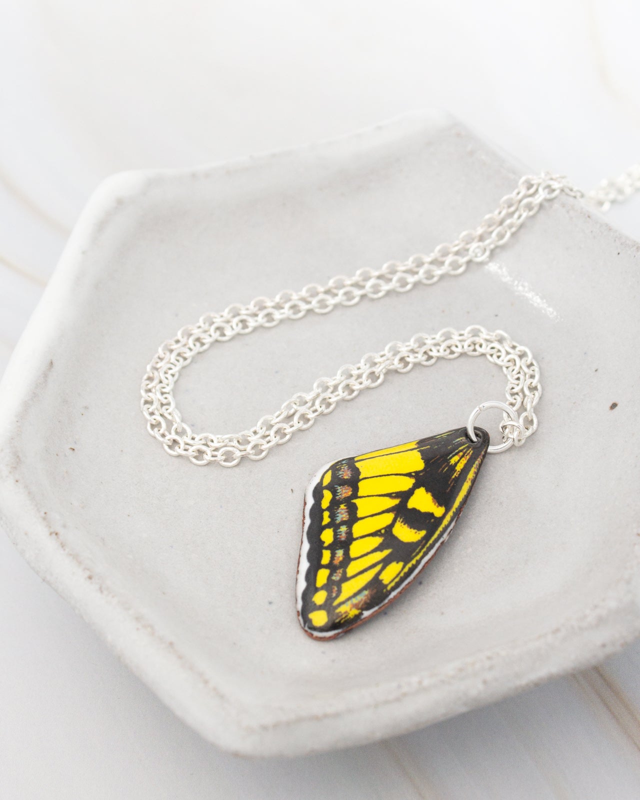 A necklace with a pendant featuring a yellow and black butterfly wing is displayed on a white plate.