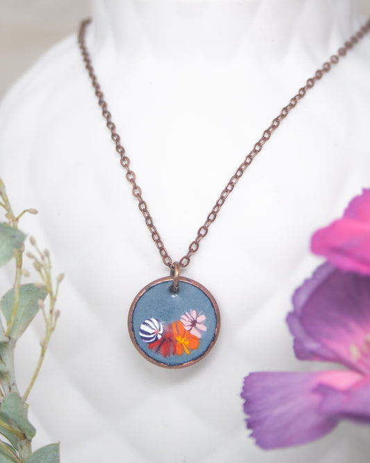 A necklace with a circular pendant featuring a floral design, including a blue background with colorful flowers.