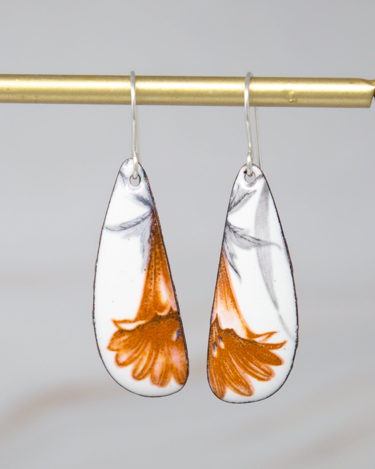 A pair of earrings with a floral design, featuring orange and white colors.