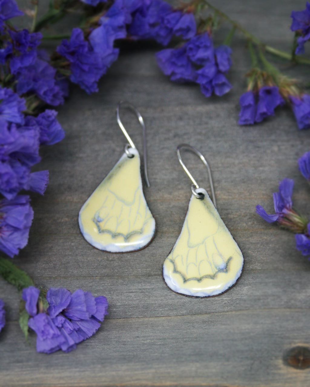 a pair of yellow and white earrings sitting next to purple flowers