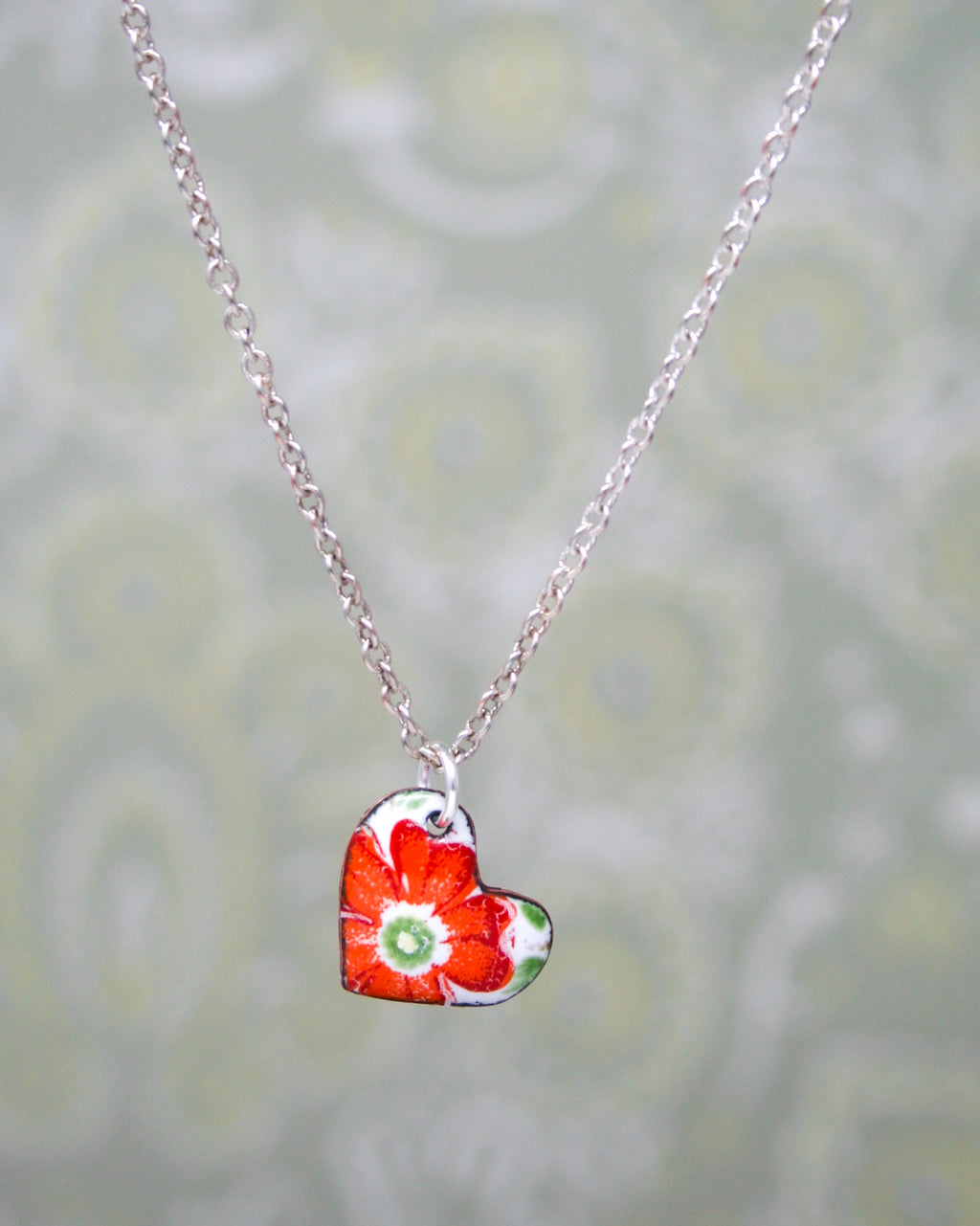 A silver necklace with a heart-shaped pendant featuring a red flower design.