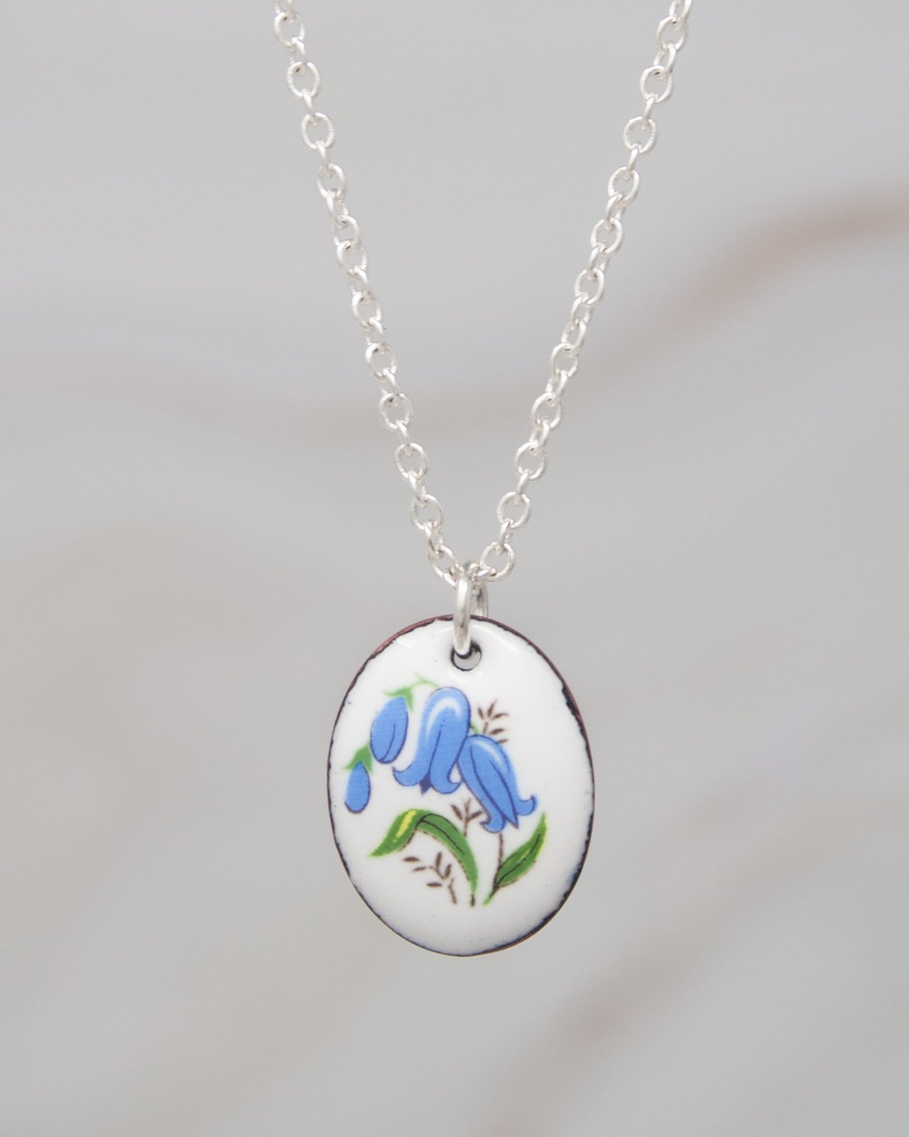 A silver necklace with a pendant featuring a blue flower design.