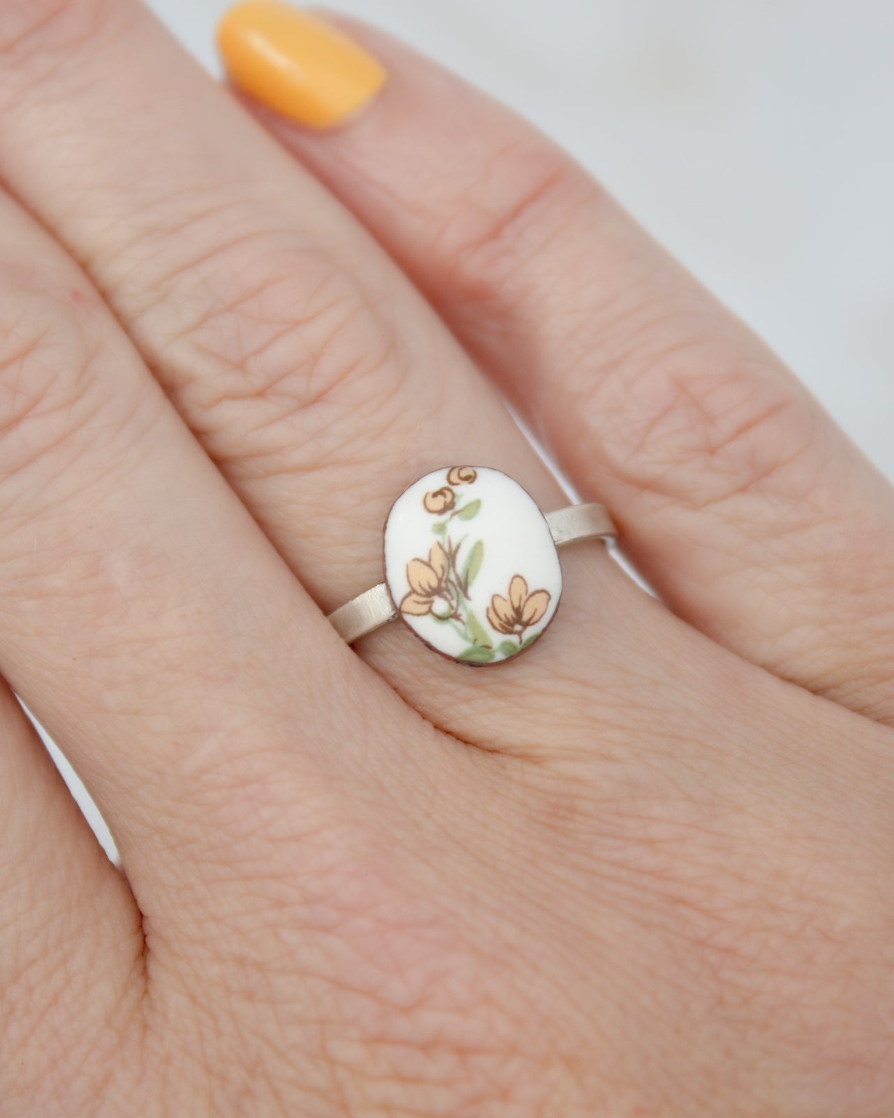 A close-up of a person's hand wearing a ring with a floral design.