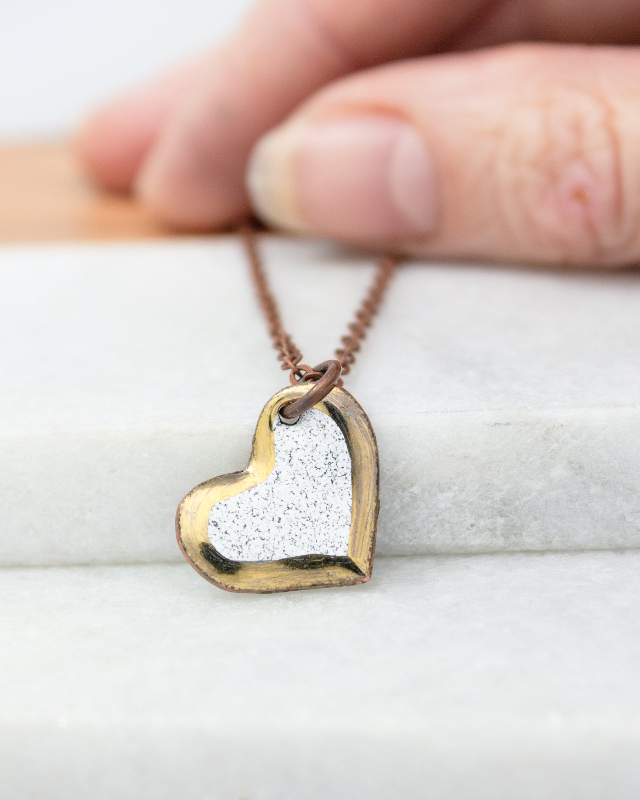 A hand is holding a heart-shaped pendant necklace with a white and gold design.