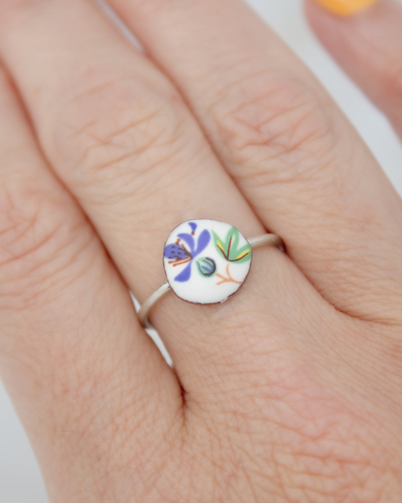 A close-up of a person's hand wearing a ring with a colorful floral design on it.