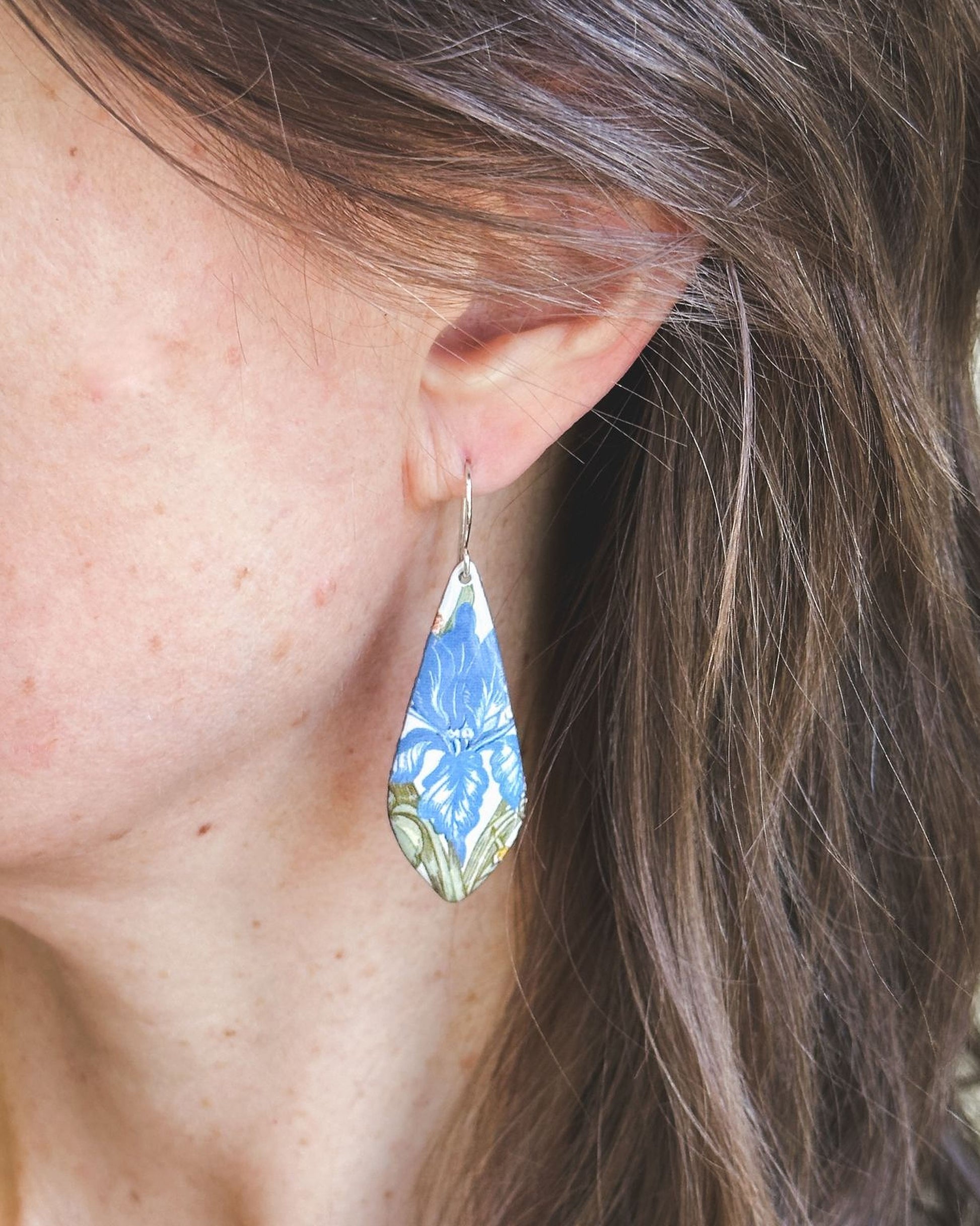 A close-up view of a person's ear wearing a blue and white floral earring.
