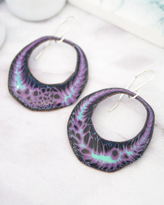 A pair of purple and black earrings with a unique, abstract design featuring a swirling pattern of purple and black lines.