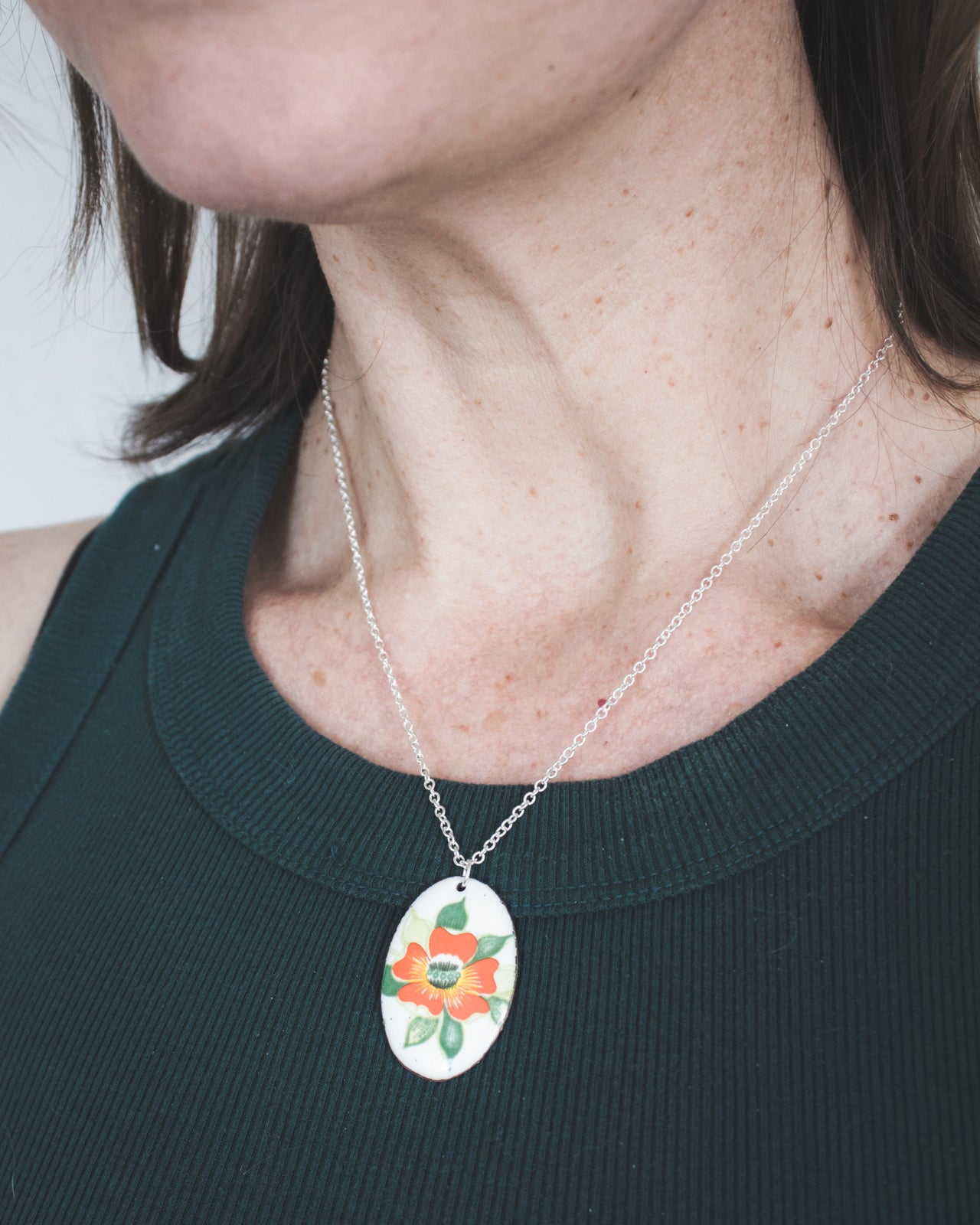 A woman wearing a green top and a necklace with a pendant featuring a flower design.