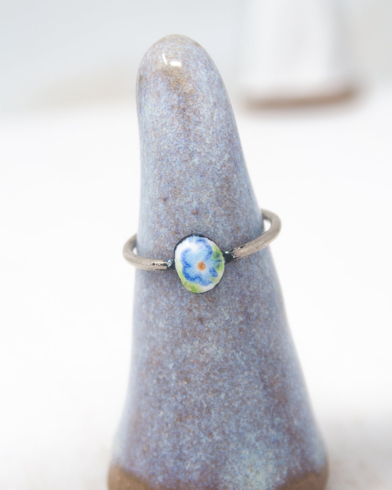 A ring with a blue stone in the center, placed on a gray ceramic stand.