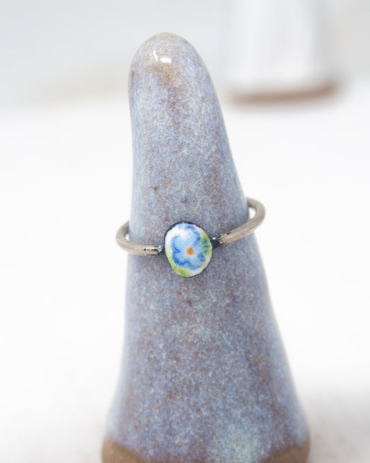 A ring with a blue stone in the center, placed on a gray ceramic stand.