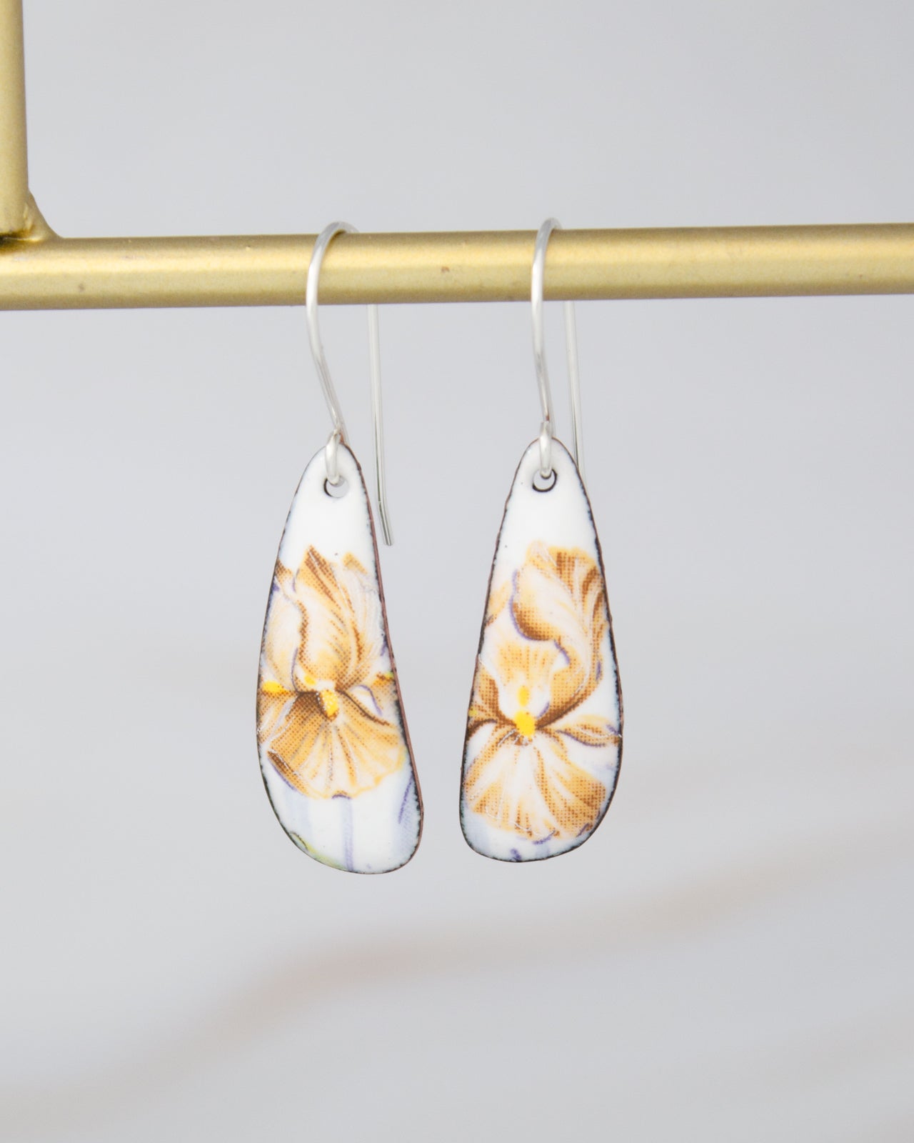 A pair of white earrings with yellow floral designs hanging from a gold metal hook.