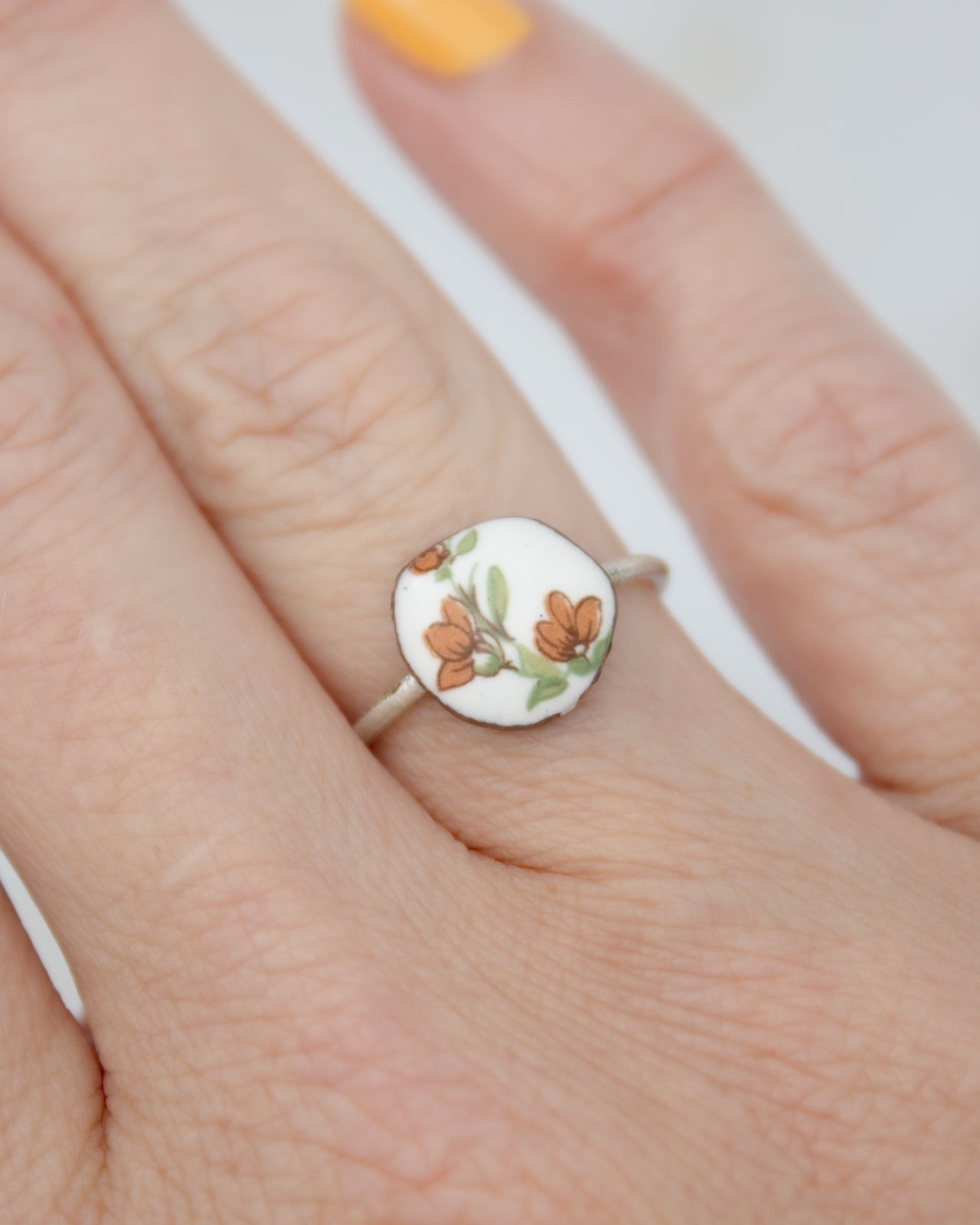 A close-up of a person's hand wearing a ring with a floral design on the finger.