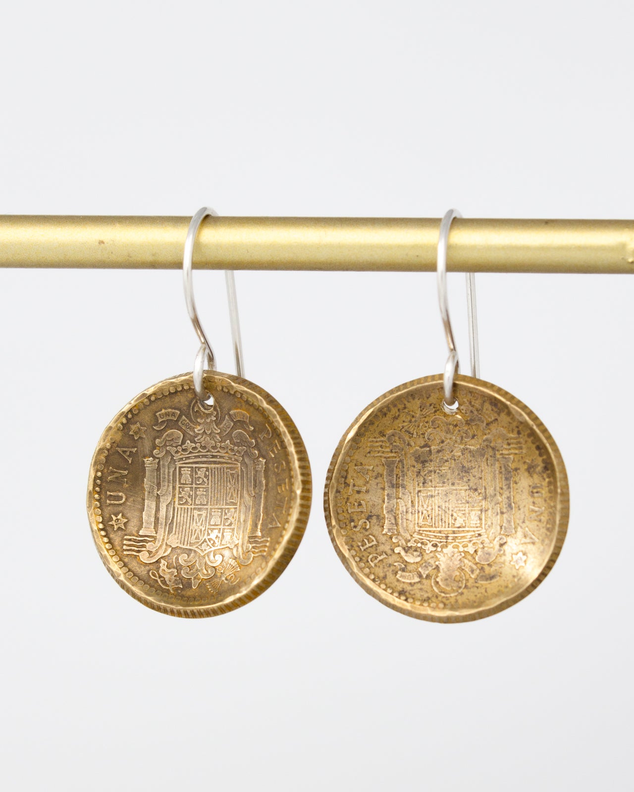 a pair of gold-colored earrings hanging from a gold-colored metal bar.