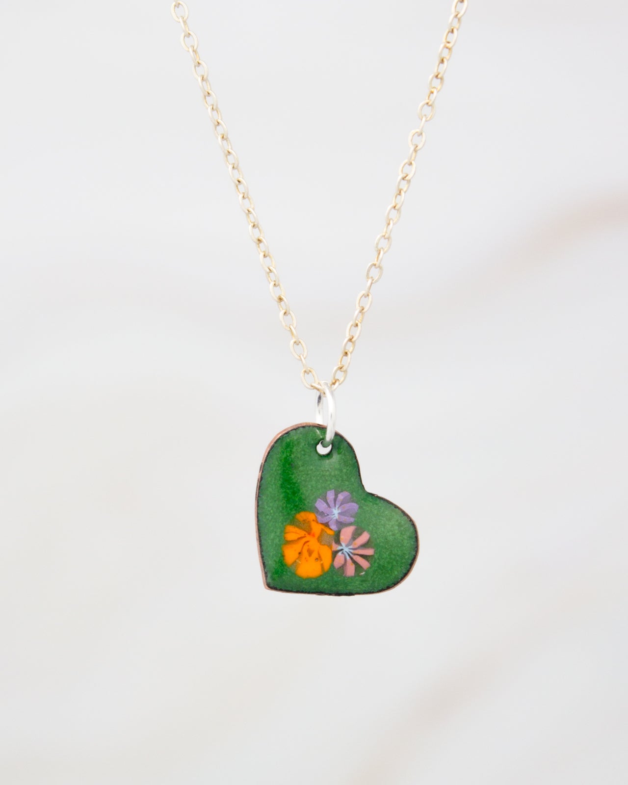 A green heart-shaped pendant with colorful flowers attached to a chain necklace.