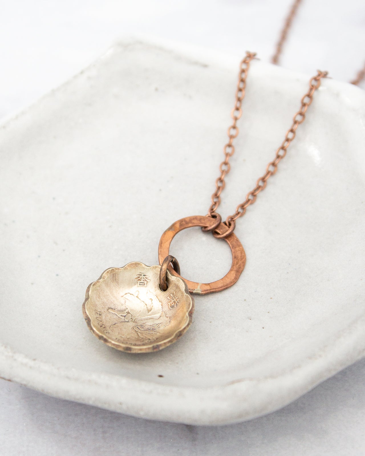 A necklace with a round pendant featuring an engraved design, hanging from a chain with a circular clasp.