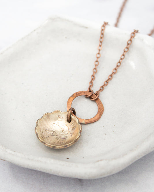 A necklace with a round pendant featuring an engraved design, hanging from a chain with a circular clasp.