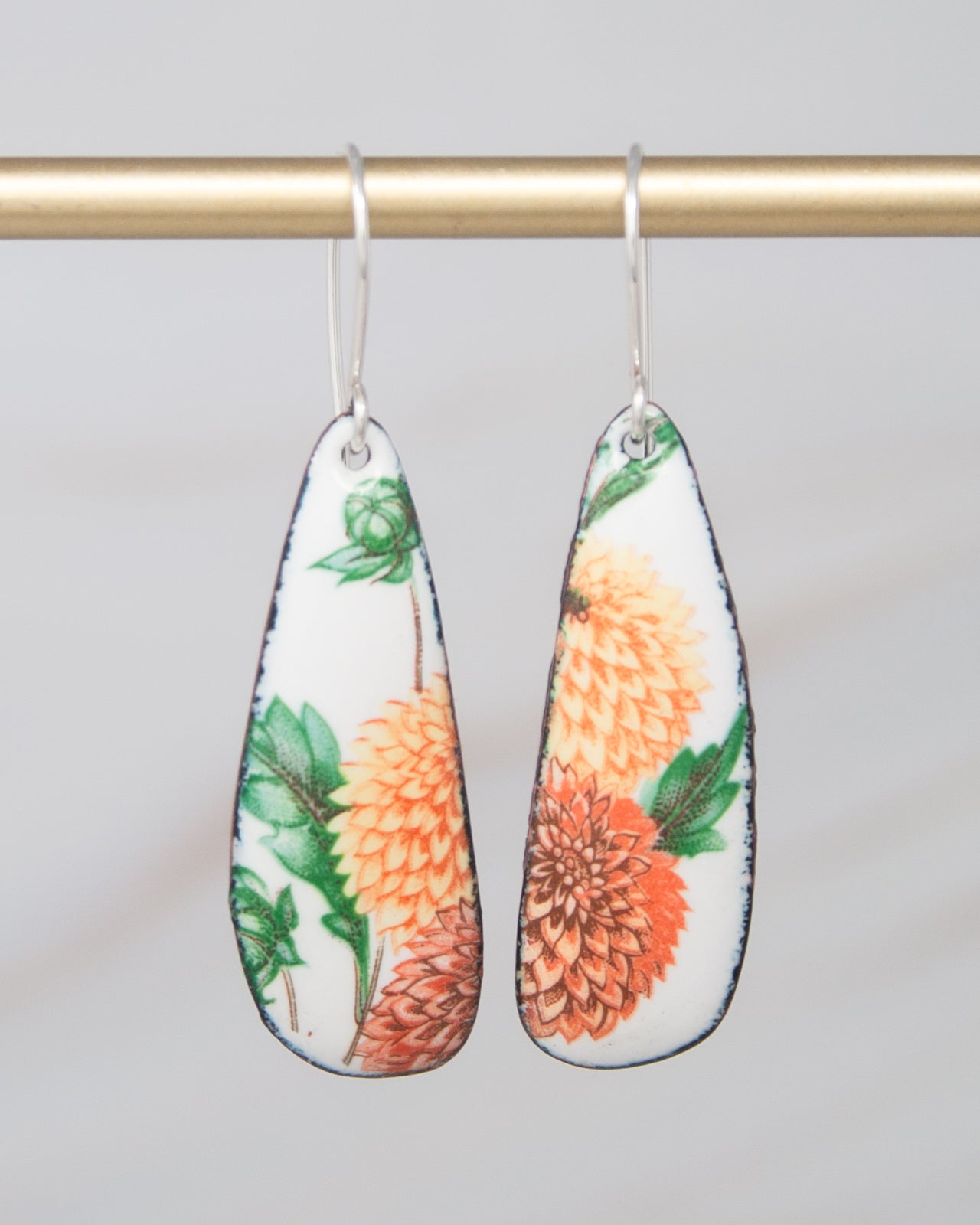 A pair of earrings with a floral design, featuring orange and green flowers on a white background.