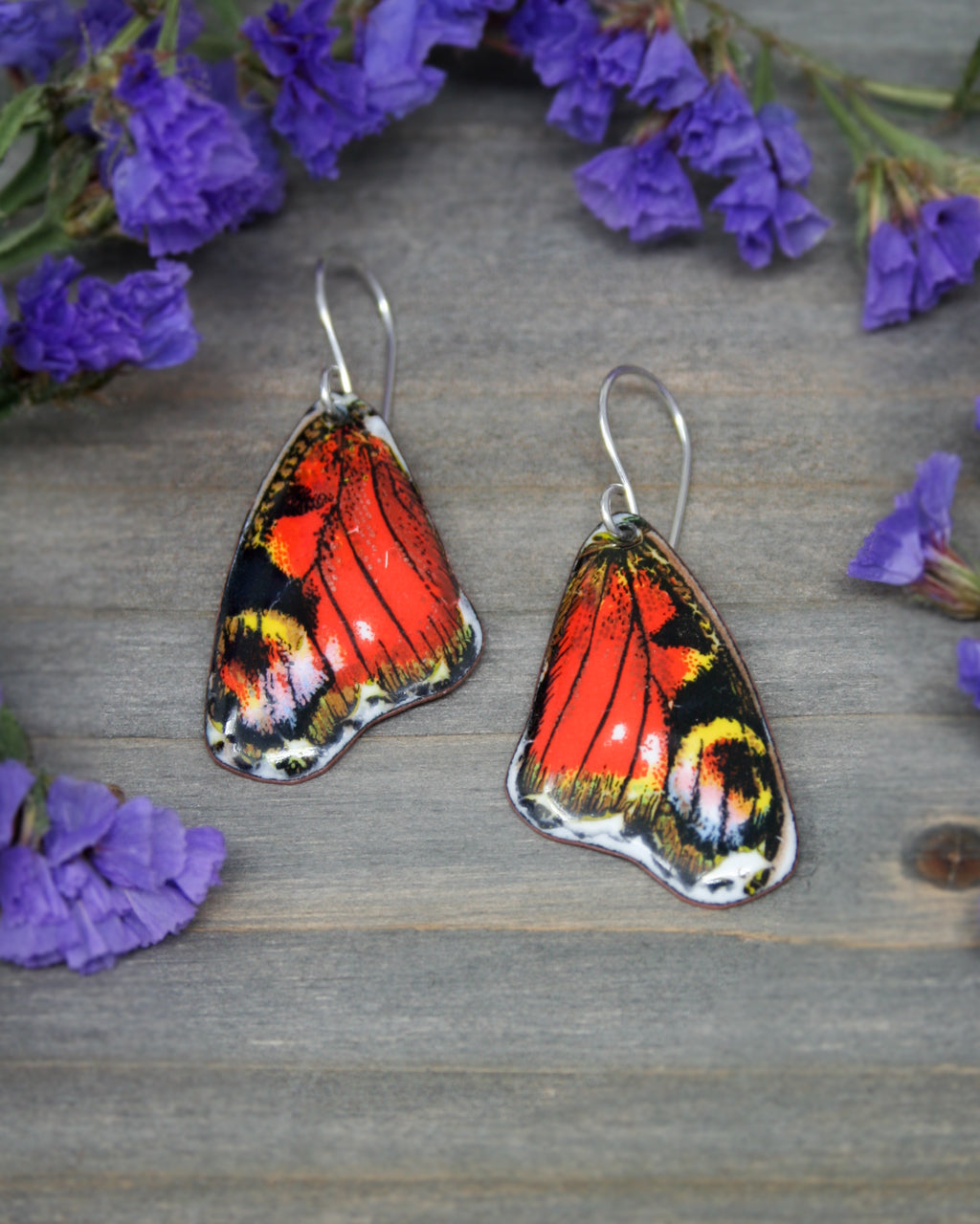 a pair of butterfly shaped earrings sitting on top of purple flowers