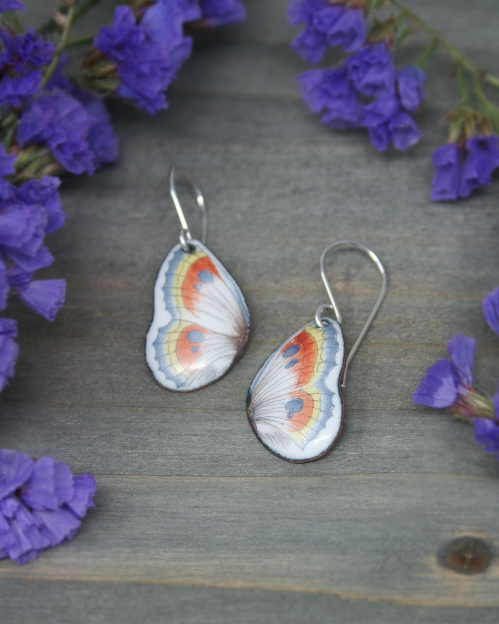 a pair of butterfly shaped earrings sitting on top of purple flowers