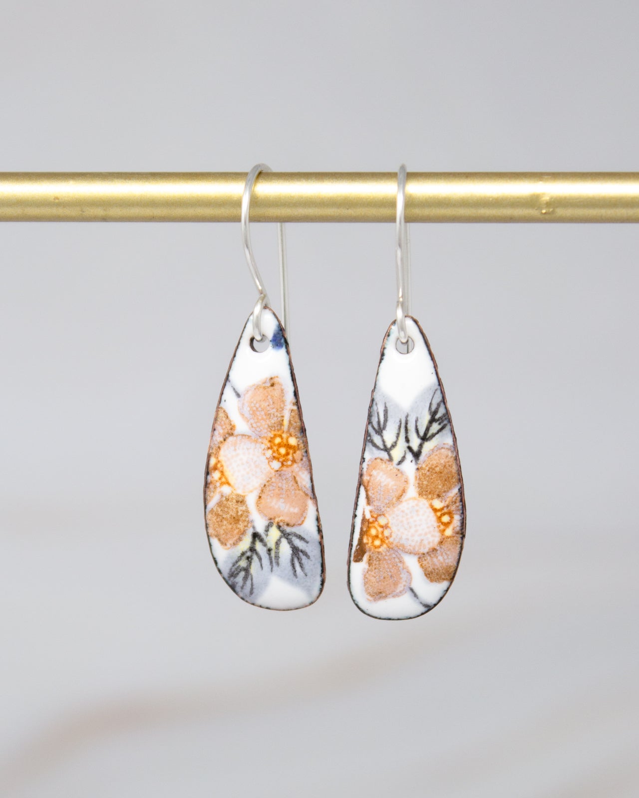 A pair of earrings with a floral design hanging from a gold-colored metal bar.