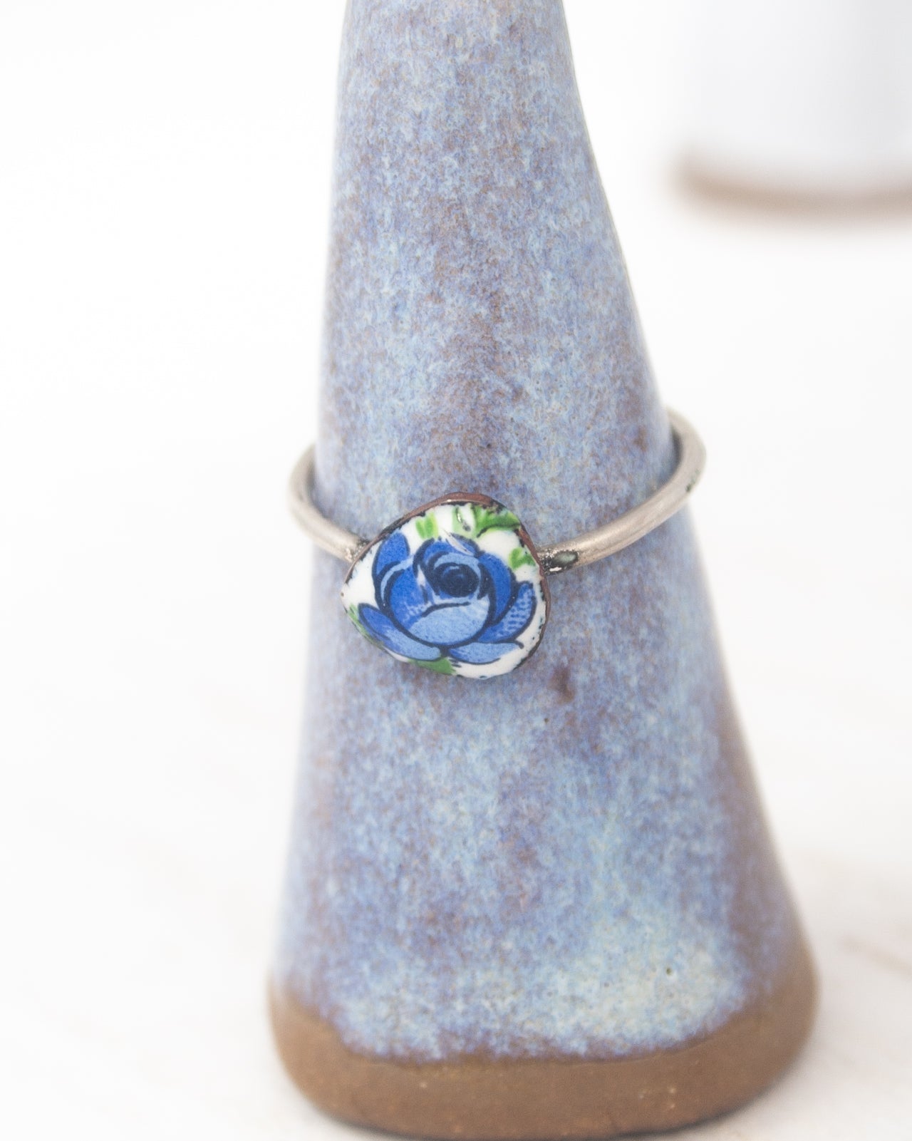 A ring with a blue flower design on it, placed on a blue and brown ceramic stand.