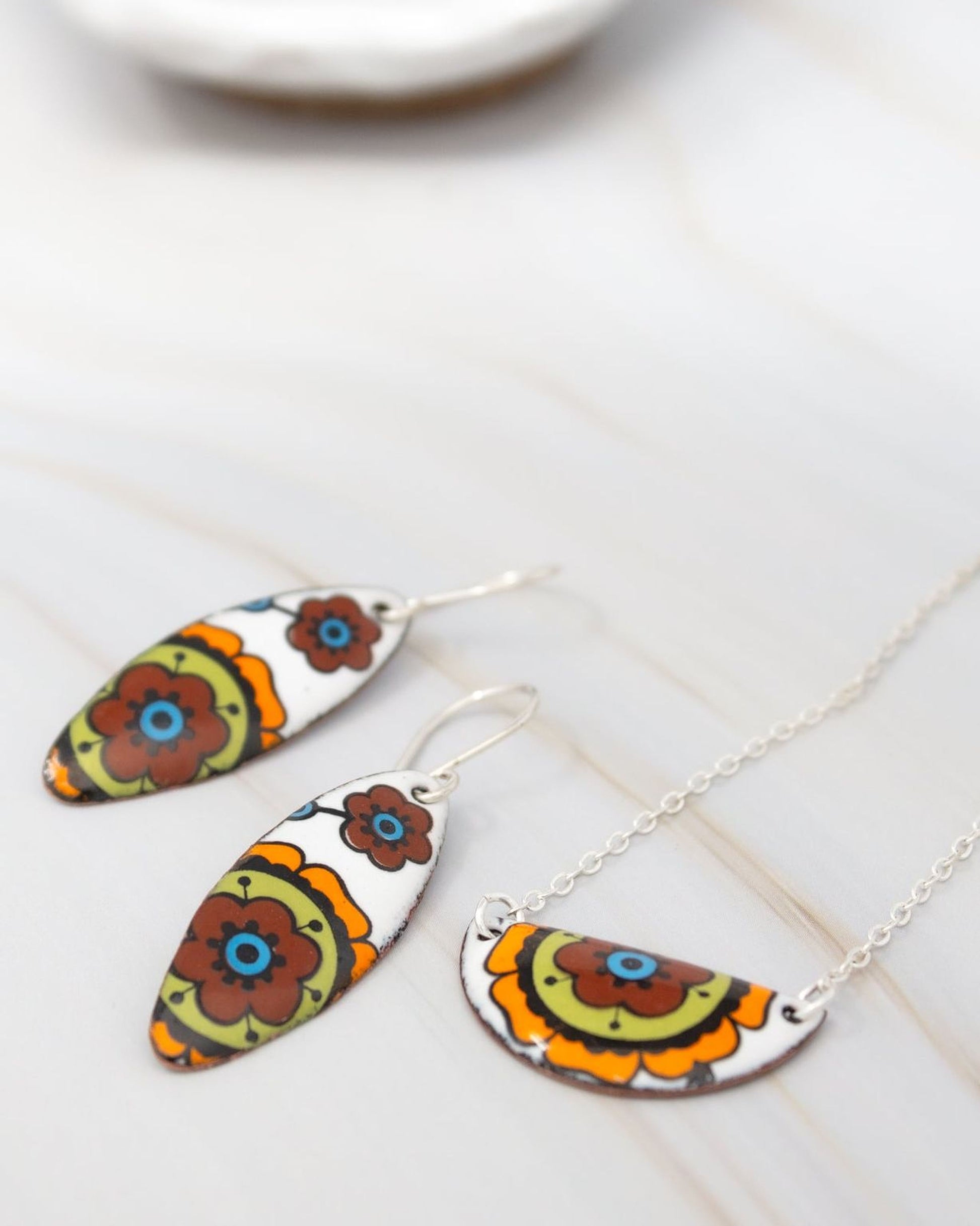 a pair of colorful earrings and a necklace with a floral design, placed on a white marble surface.
