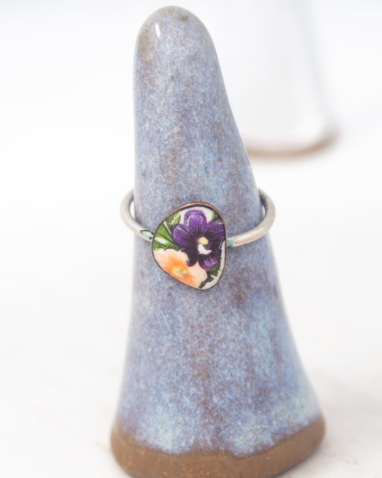 A ring with a floral design is displayed on a blue ceramic ring holder.