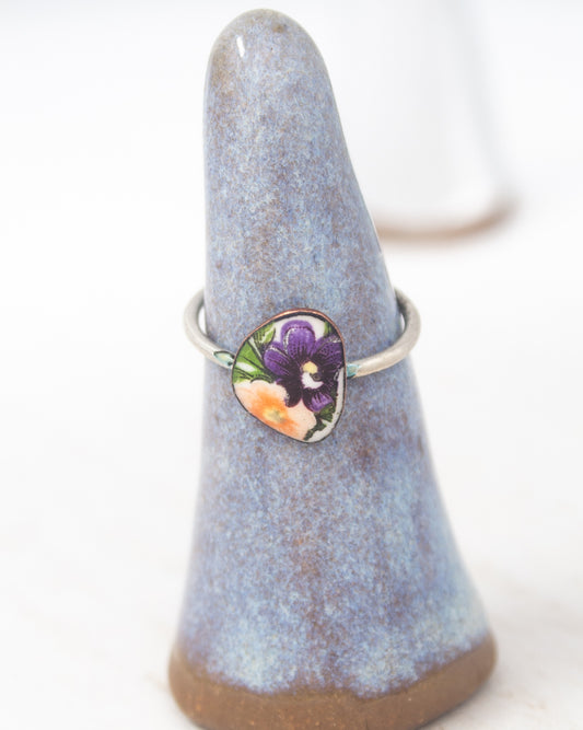 A ring with a floral design is displayed on a blue ceramic ring holder.