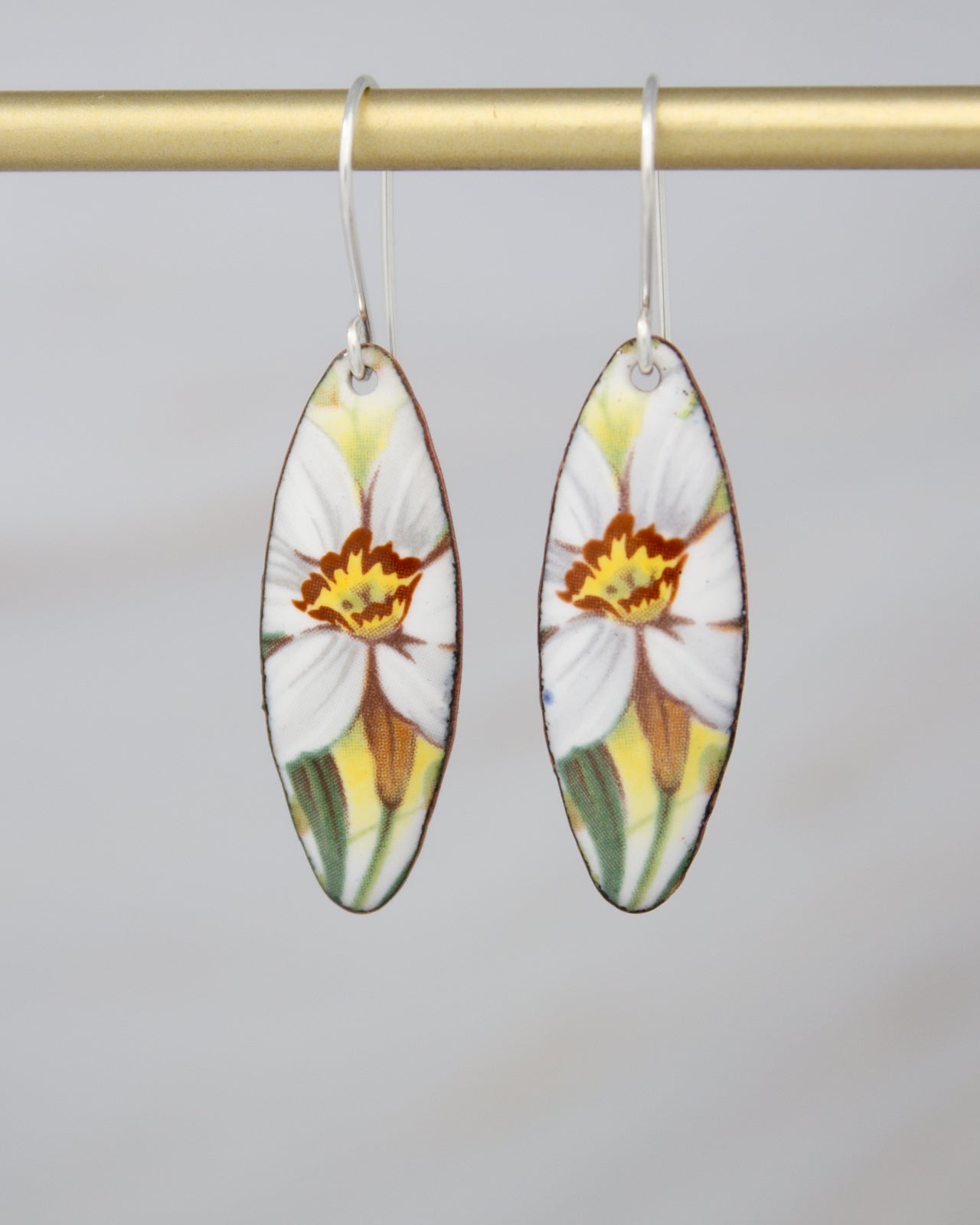 A pair of earrings with a floral design, featuring white and yellow flowers with green leaves.