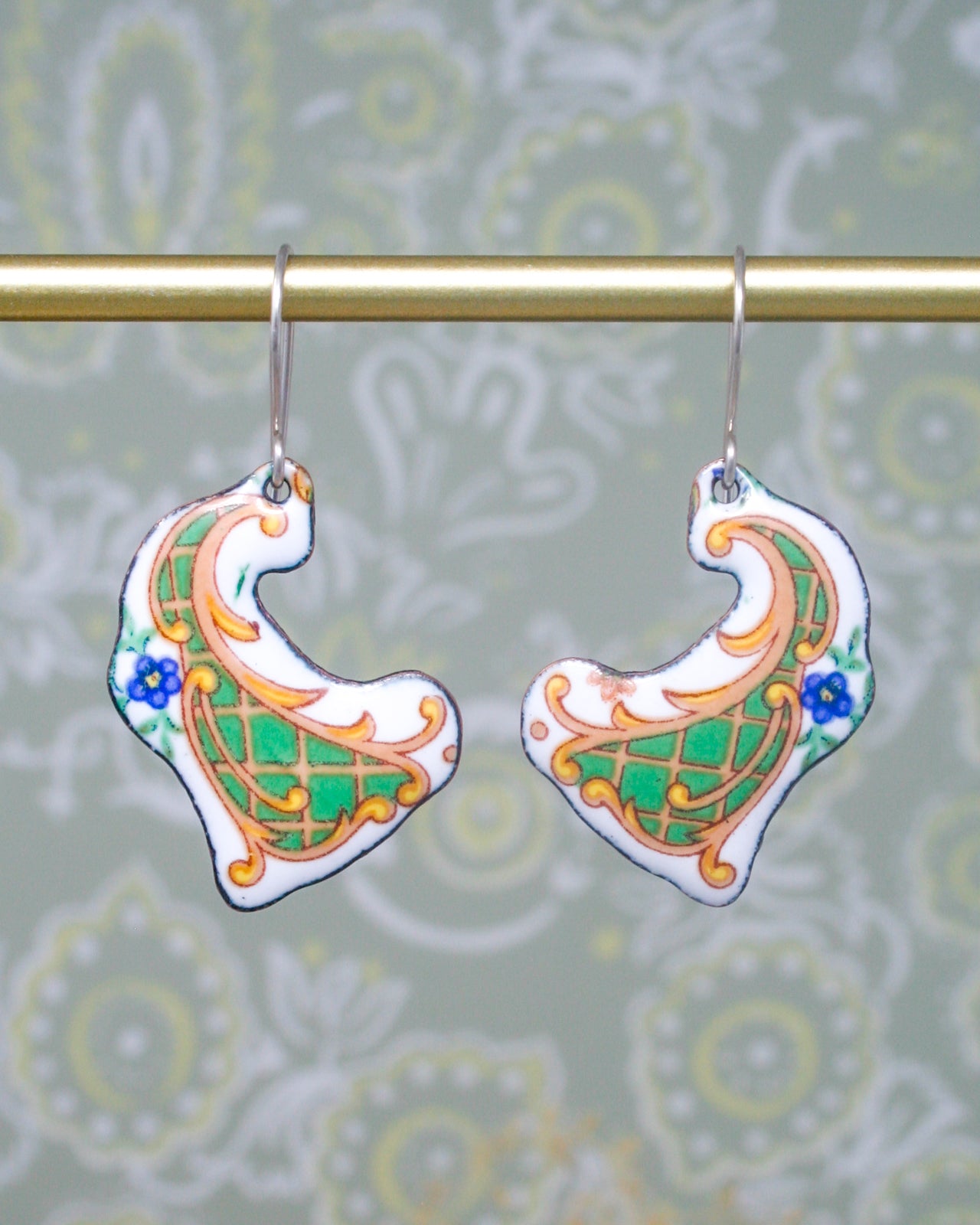 A pair of ornate earrings with intricate designs, hanging from a gold-colored metal hook.