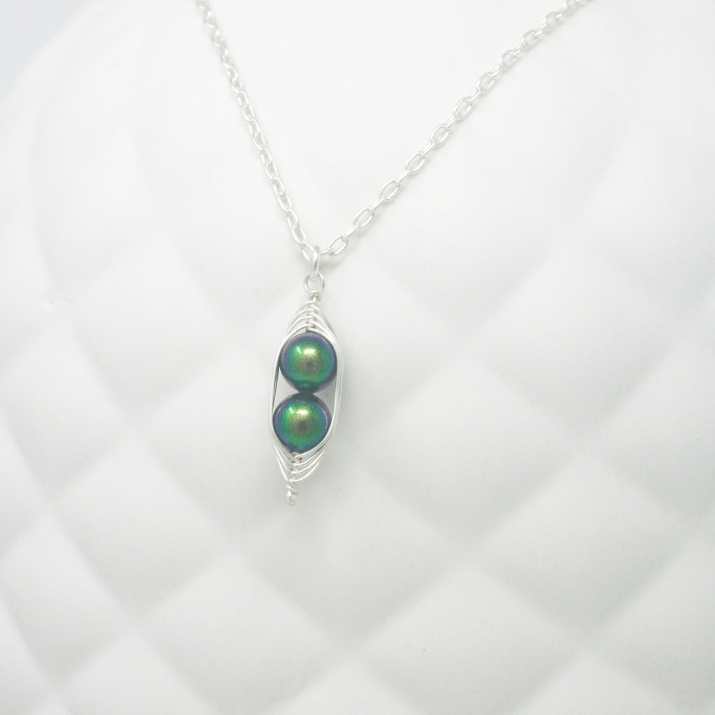 a silver necklace with two green pearls hanging from it