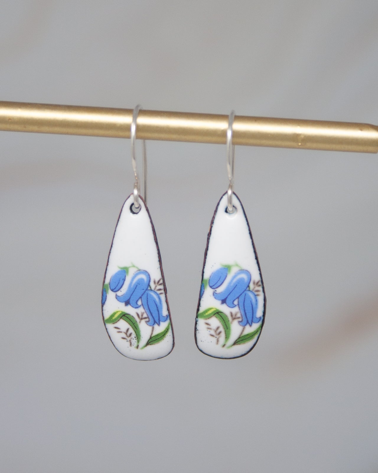 A pair of earrings with blue flowers on a white background, hanging from a gold bar.