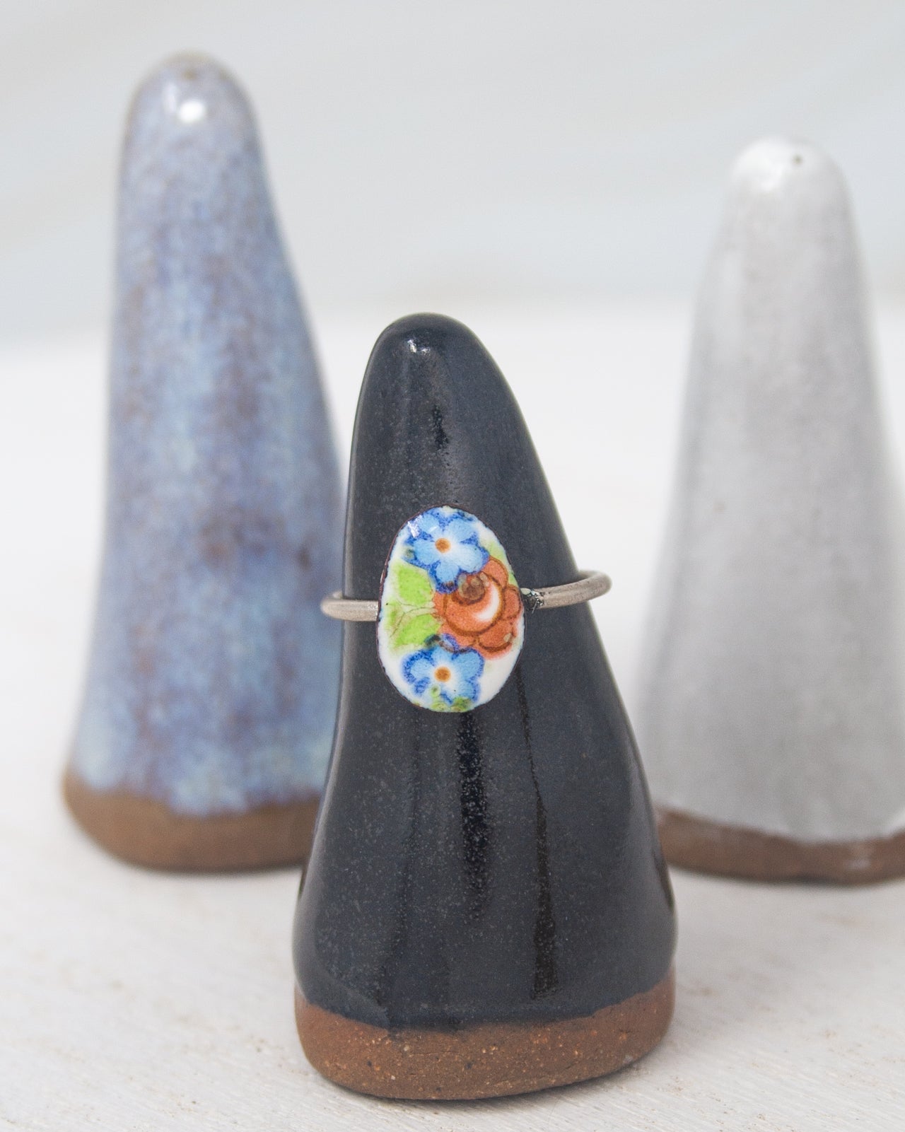 A black ceramic ring stand with a colorful floral design on it, placed between two white ceramic holders.