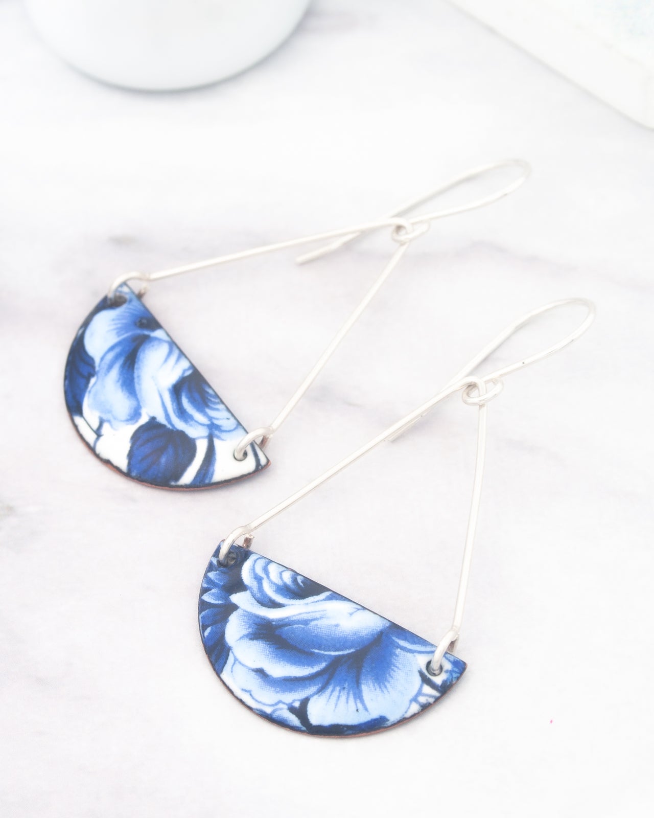 A pair of earrings with blue floral designs on a white marble surface.