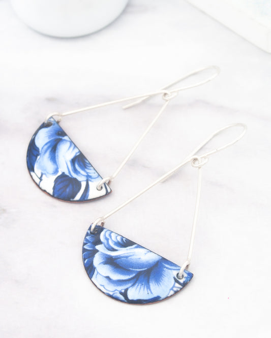 A pair of earrings with blue floral designs on a white marble surface.
