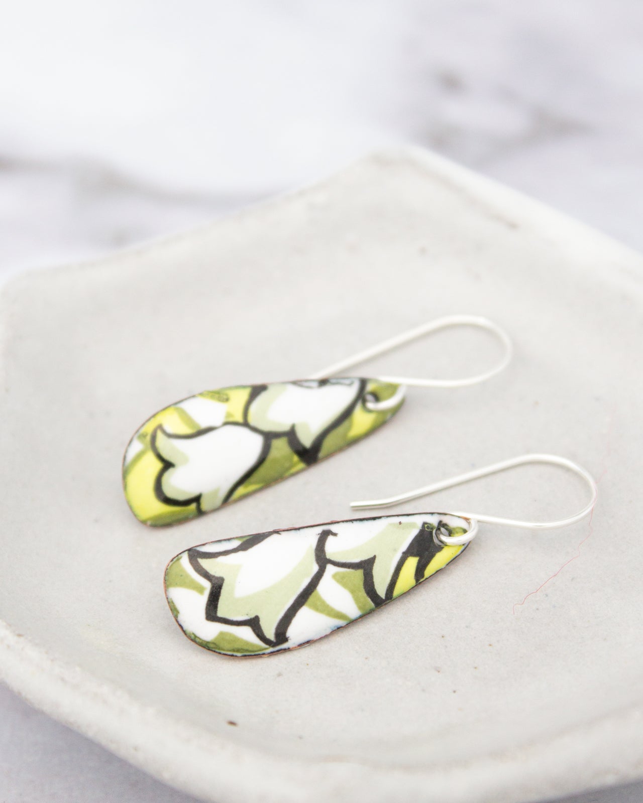 A pair of earrings with a green and white floral pattern on a white plate.