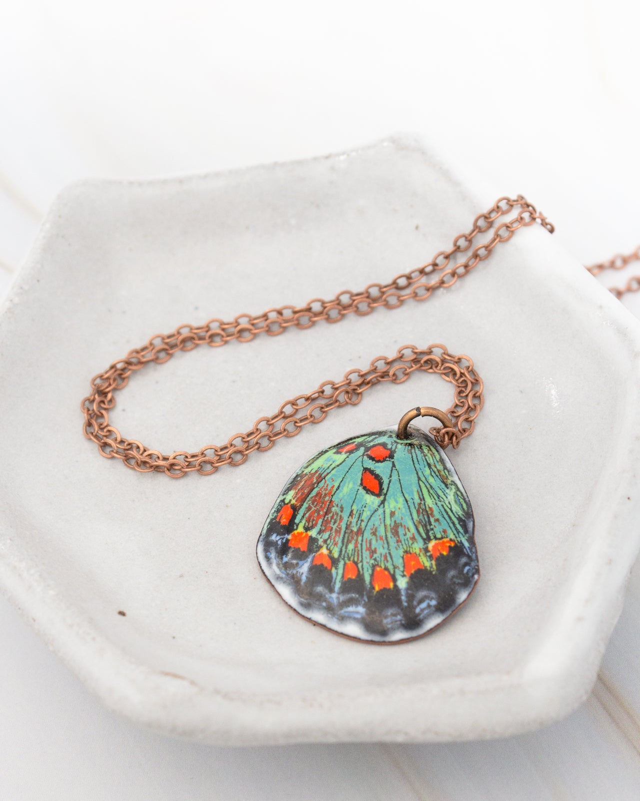 A necklace with a pendant featuring a colorful butterfly design rests on a white plate.