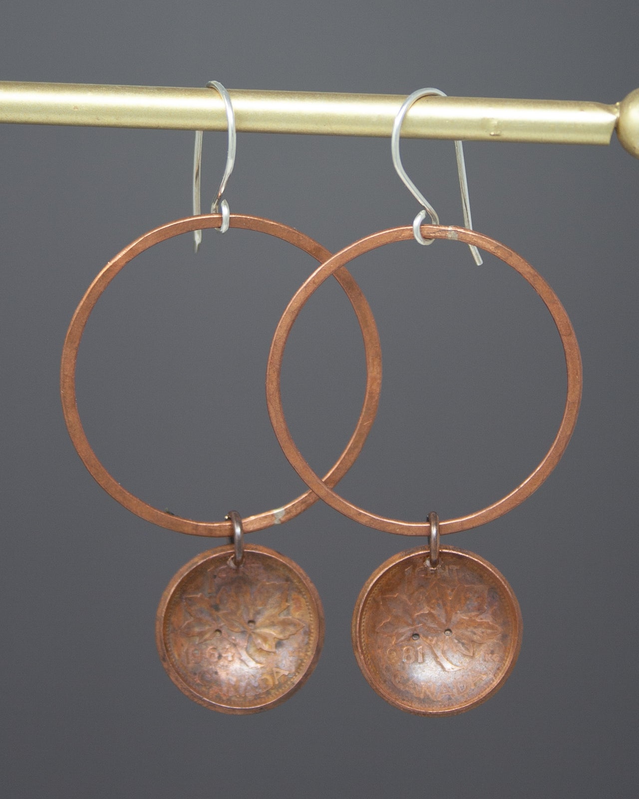 A pair of copper-colored earrings with circular metal discs hanging from the bottom of the hoop.