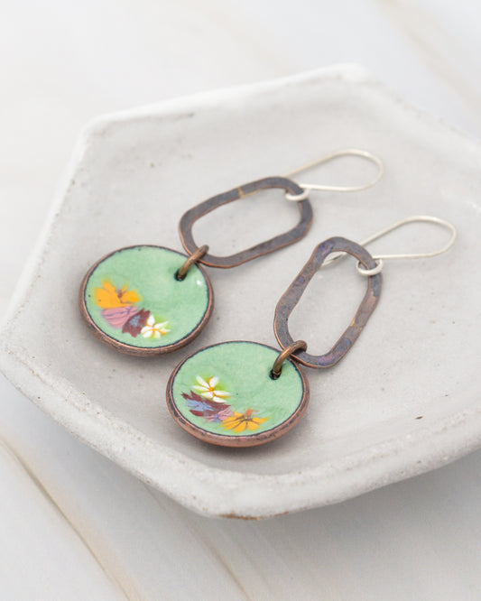 A pair of green earrings with flower designs on them, displayed on a white plate.