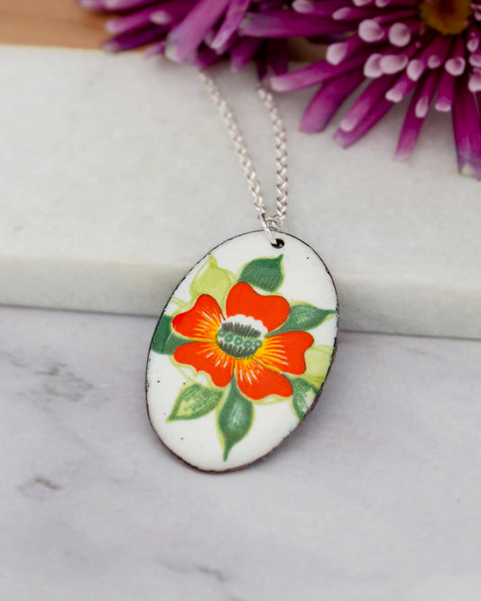 A necklace with a pendant featuring a colorful flower design is displayed on a white surface.