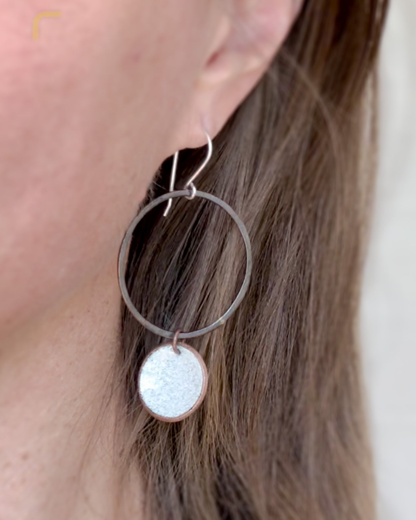 A close-up view of a person's ear wearing a pair of silver hoop earrings with a small circular charm hanging from them.