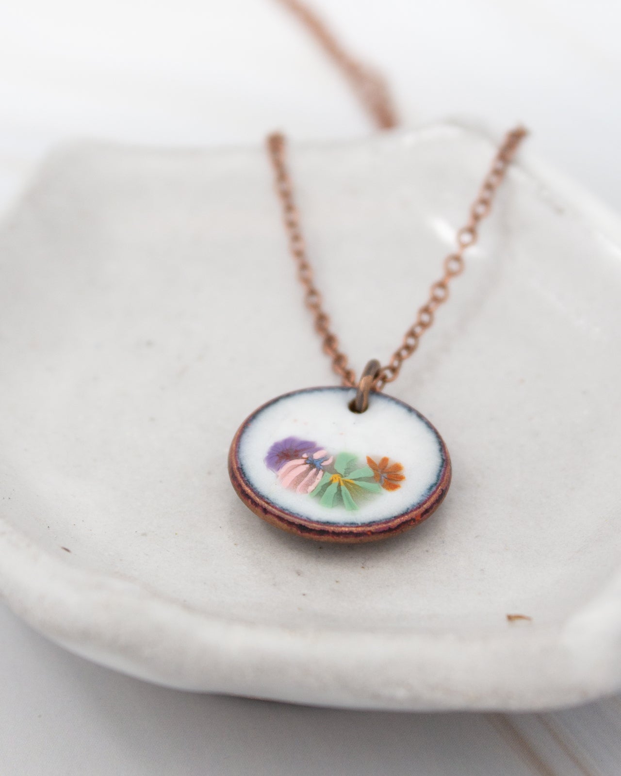 A necklace with a circular pendant featuring a floral design is displayed on a white plate.