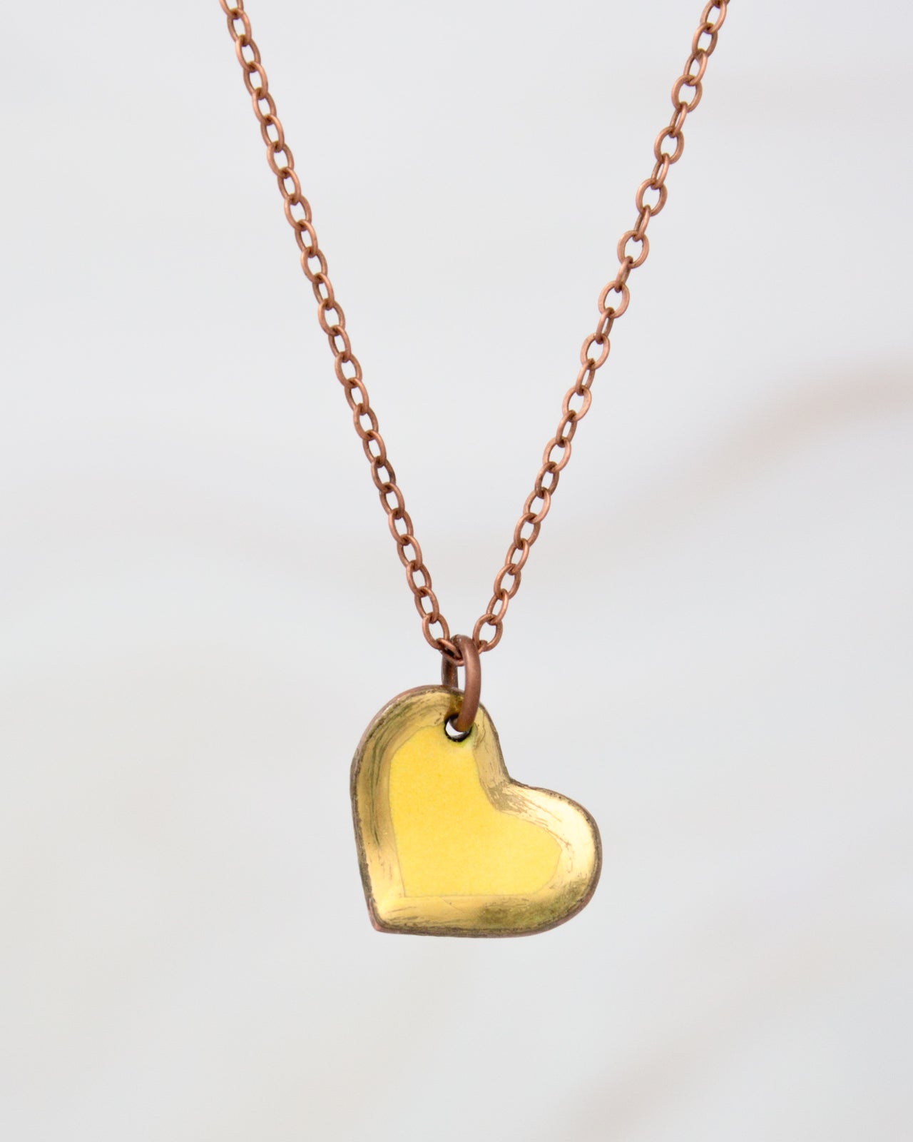 A delicate gold heart-shaped pendant necklace with a copper-colored chain.
