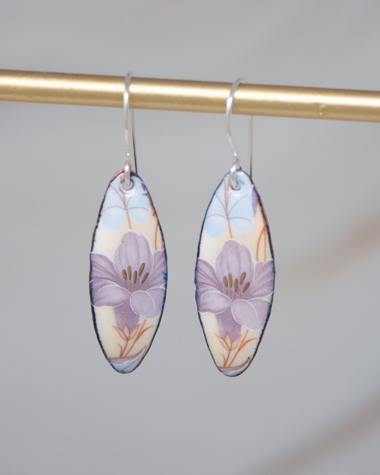 A pair of earrings with a floral design, featuring two oval-shaped pendants with purple and blue flowers.