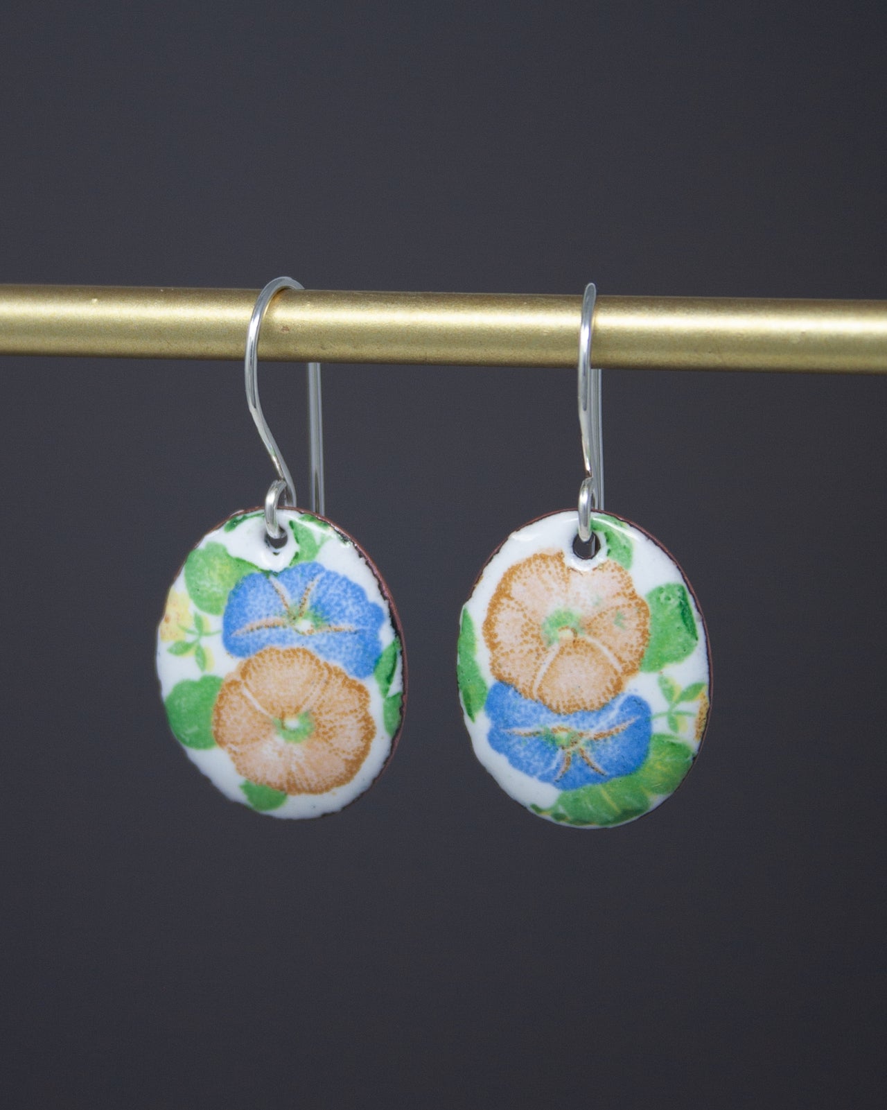 A pair of earrings with a floral design, featuring blue and orange flowers on a white background.